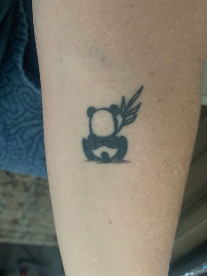 A minimalist tattoo of a panda holding a leaf on an arm, representing personal expression.