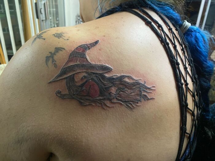 Tattoo of a witch flying on a broomstick, with a pointed hat, located on someone's shoulder.