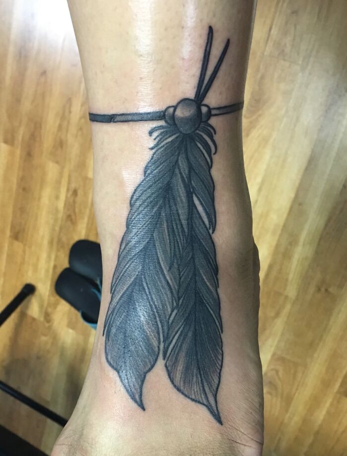 A detailed feather tattoo on an ankle, showcasing intricate shading and line work.