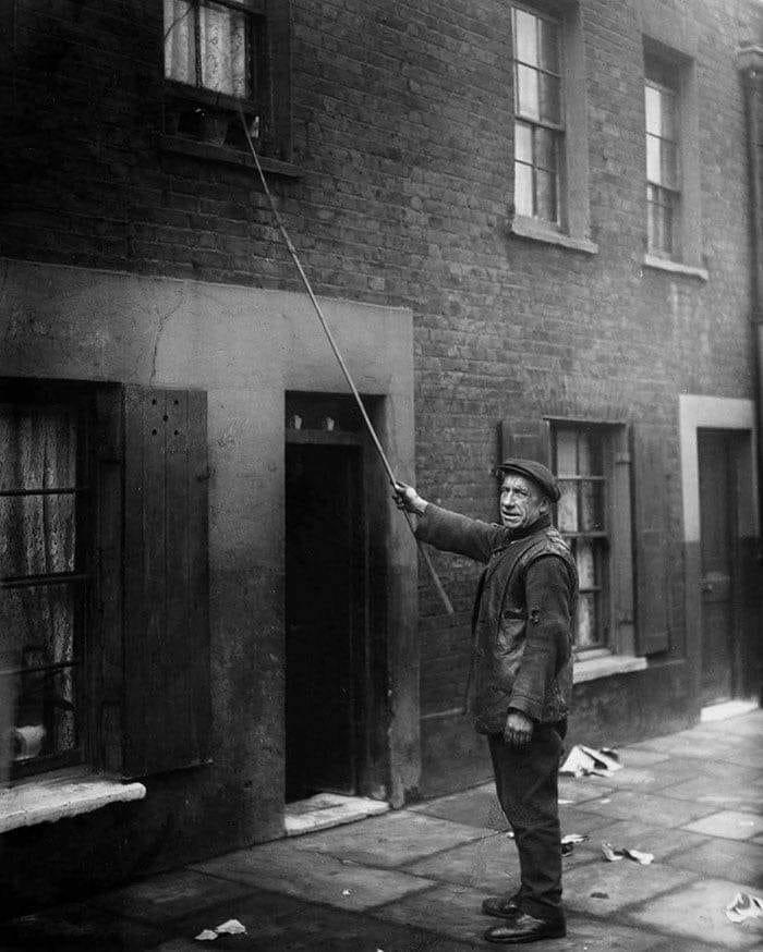 Un hombre tocando la ventana en Londres (1929). Antes de que existieran los despertadores, se pagaba por despertar a los clientes para que trabajaran llamando a sus puertas y ventanas con un palo