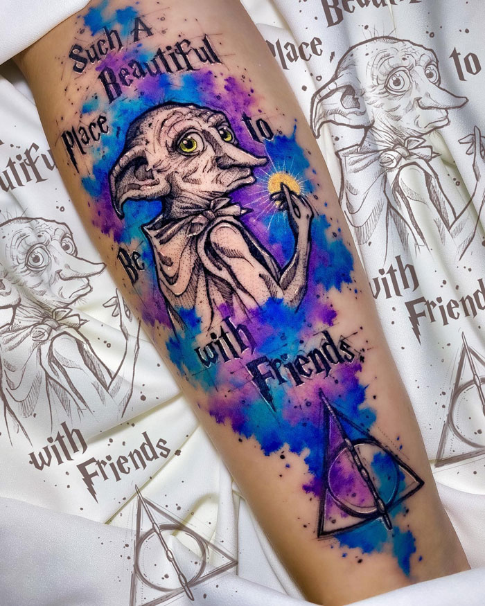 Harry Potter tattoo featuring Dobby, colorful watercolor background, and Deathly Hallows symbol on a person's arm.