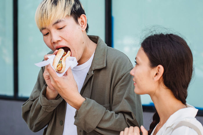 Man eating hotdog and woman watching