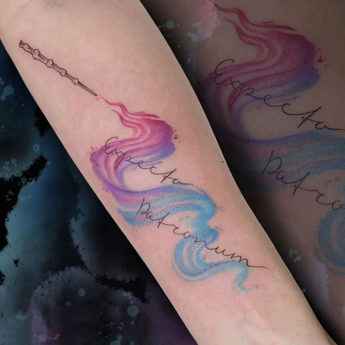 Ink tattoo of "Expecto Patronum" and a wand, featuring colorful swirls on arm; Harry Potter tattoo inspiration.