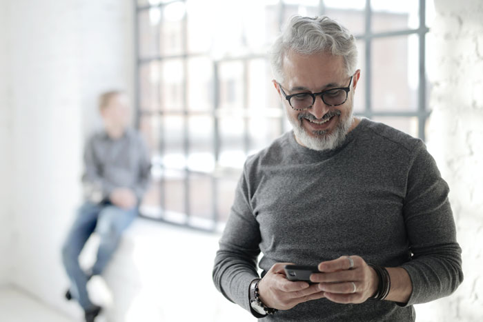 Man wearing gray shirt watching phone and smiling