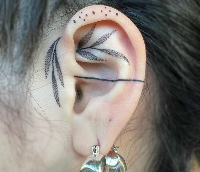 Ear with delicate leaf tattoo art and dotted accents, black ink.