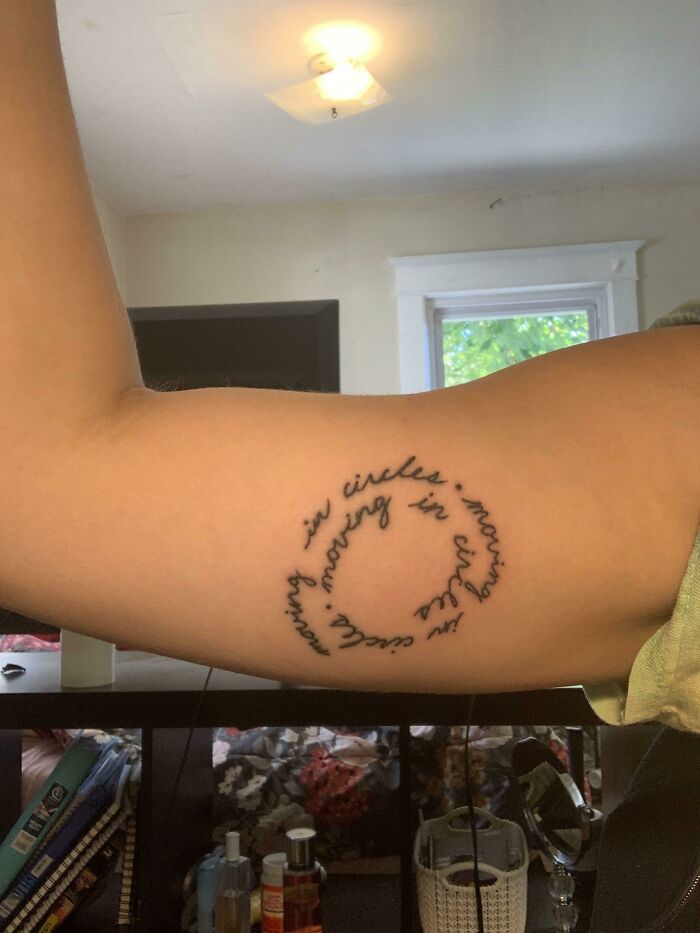 Circular script word tattoo on inner arm in bright room setting.
