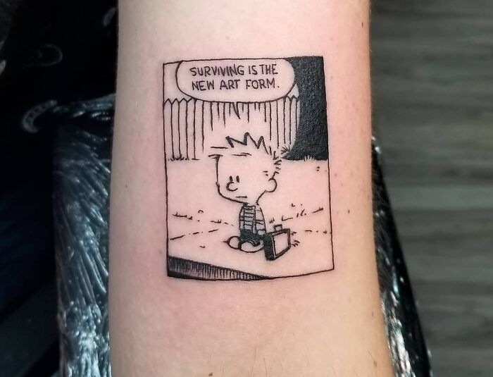 Cartoon character tattoo with text "Surviving is the new art form" on forearm, reflecting deep word tattoo inspiration.