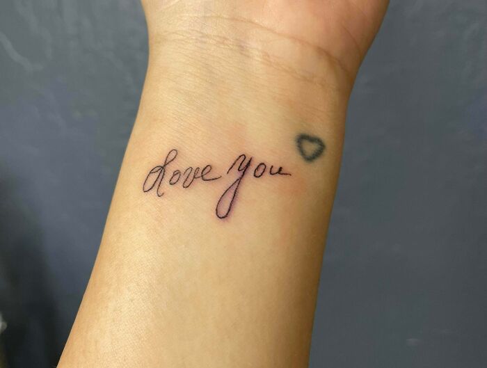 Tattoo of "love you" in elegant script on a wrist with a small heart outline, highlighting meaningful word tattoos.