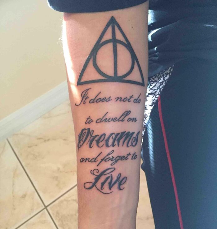 Arm tattoo featuring the Deathly Hallows symbol and the quote "It does not do to dwell on dreams and forget to live."