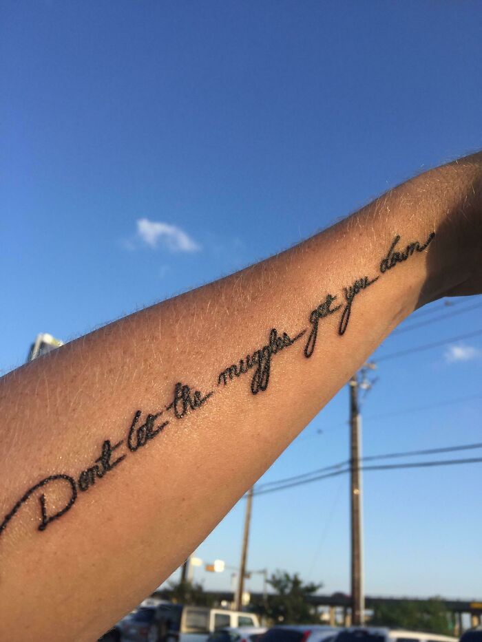 Harry Potter tattoo on arm with quote in cursive script, against a clear blue sky background.