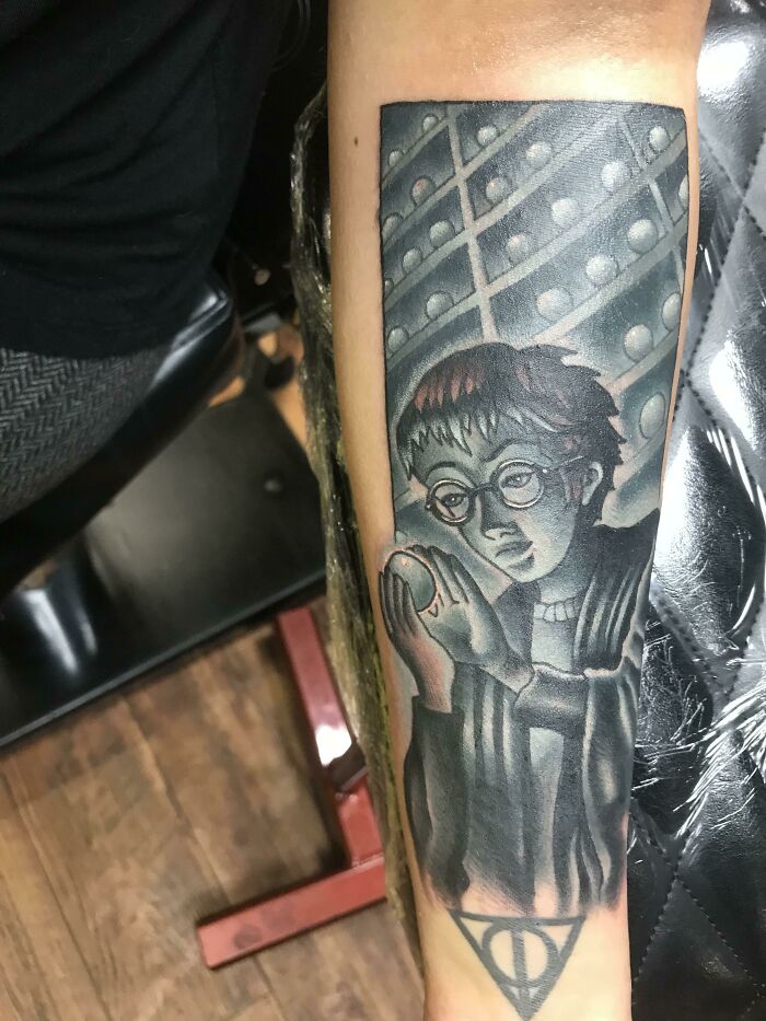 Harry Potter tattoo featuring character with glasses and the Deathly Hallows symbol, inked on forearm.