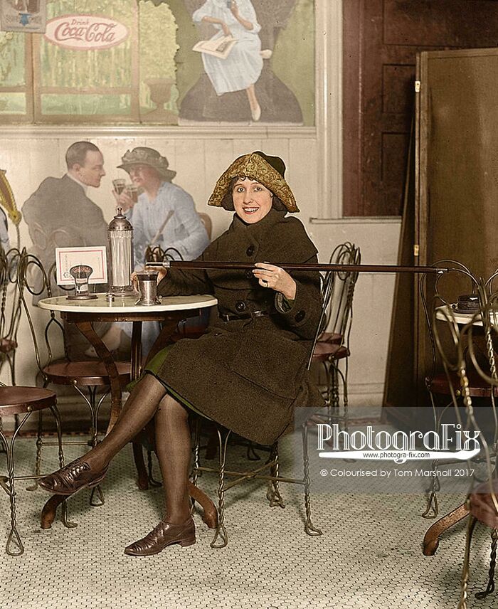 [13 de febrero de 1922] Mujer sentada en la mesa con una fuente de soda vertiendo alcohol de un bastón en un vaso