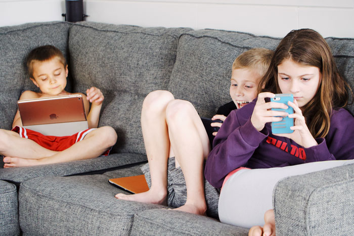 Kids sitting and playing with phones and tablets