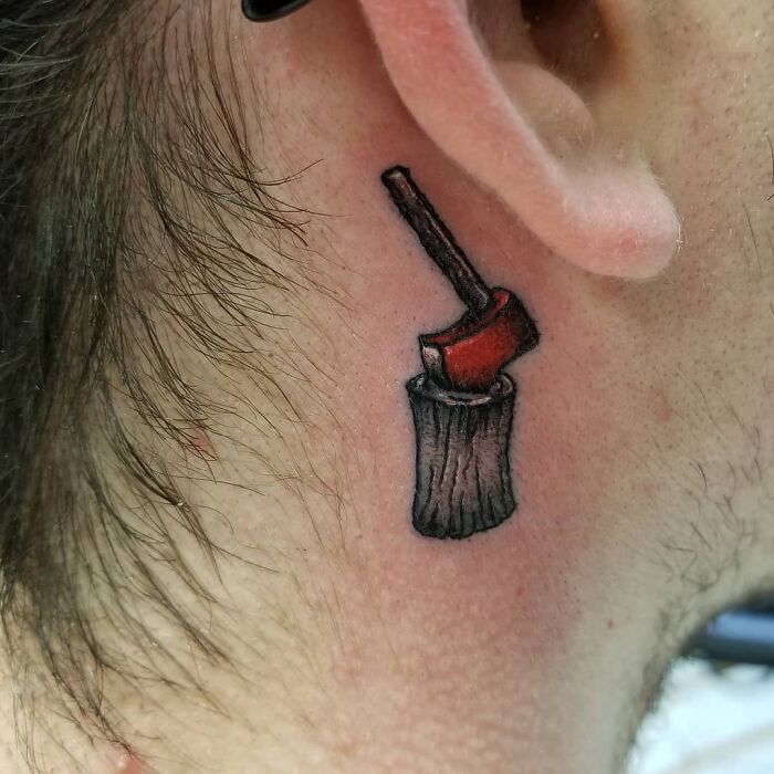 Ear tattoo of a red axe on wood, showcasing unique art style.