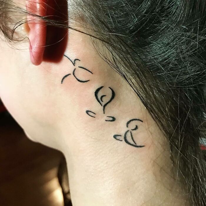 Stylized design tattoo behind the ear, featuring abstract black lines.