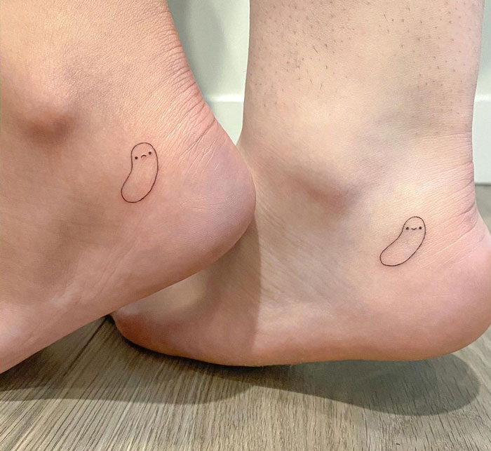 Matching minimalist best friend tattoos of small bean figures on ankles, symbolizing friendship.