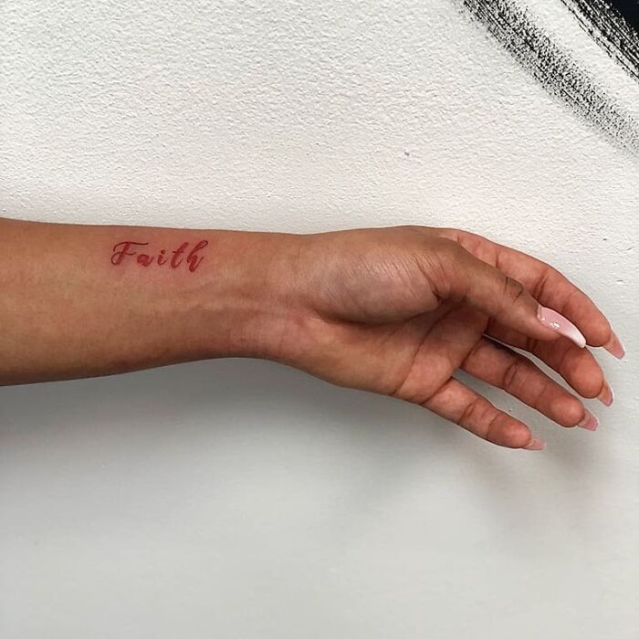 Word tattoo "Faith" on forearm, minimalist style against a white background.