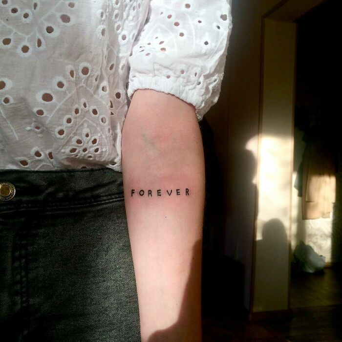 Word tattoo "forever" on arm in sunlight, wearing a white eyelet shirt.