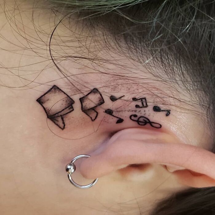 Ear tattoo featuring musical notes and geometric designs near a pierced ear.