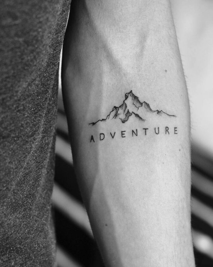 Arm tattoo with mountains and the word "ADVENTURE," representing a word tattoo that inspires exploration.