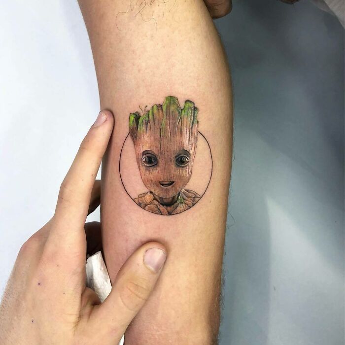 Marvel tattoo of Groot on forearm, with vibrant green and brown details highlighted by a finger pointing.