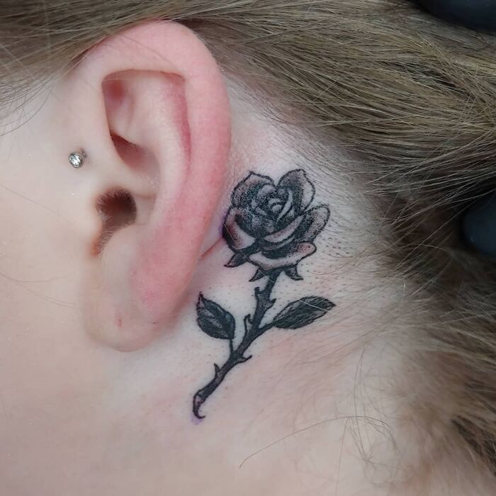 Rose tattoo behind the ear with a small stud earring visible.