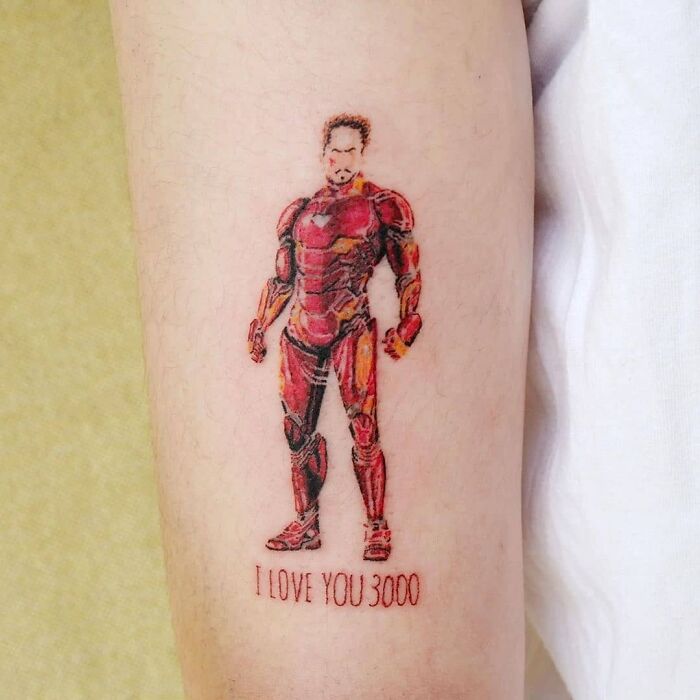 Marvel tattoo of a superhero Iron Man in red armor with the quote "I love you 3000" on an arm.