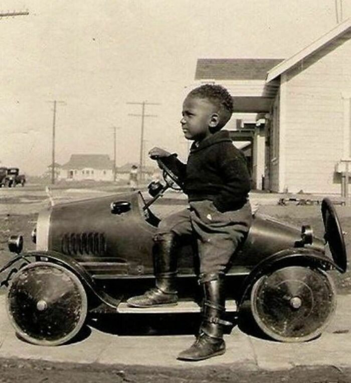 Small boy sitting in a small car in a driveway 