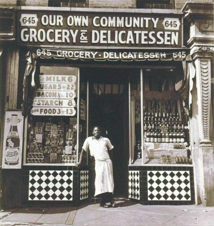 Man with an apron standing near a small grocery store 