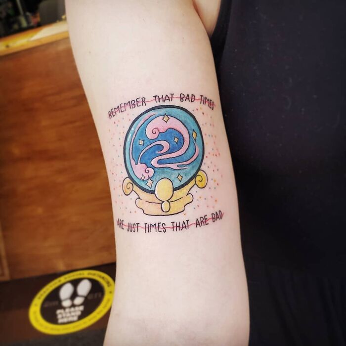 Colorful word tattoo on an arm, featuring a crystal ball design with inspirational text.