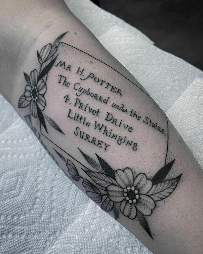 Harry Potter tattoo with address on arm, surrounded by flowers.
