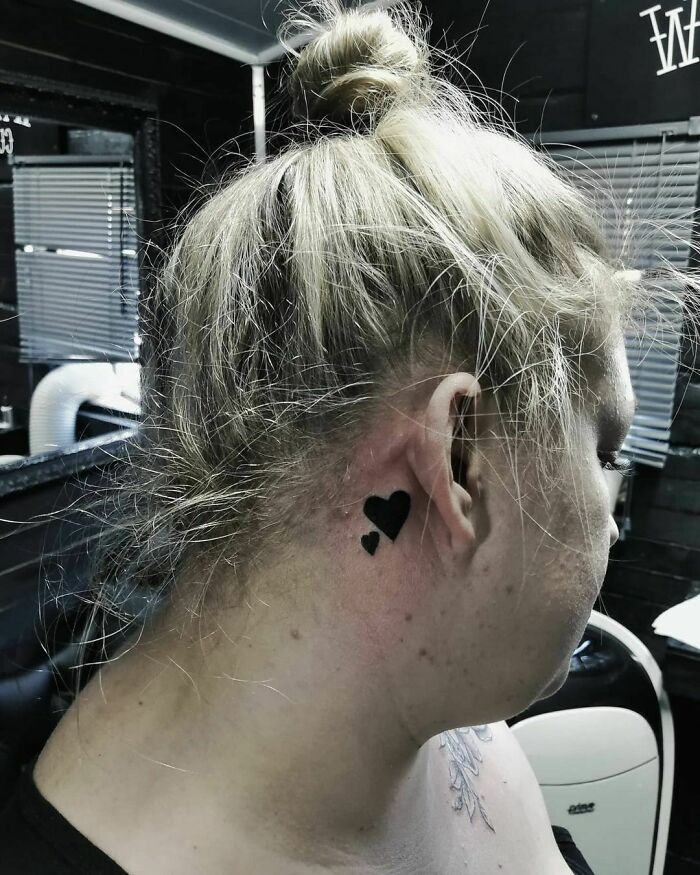 A person with heart-shaped ear tattoos in a hair bun, captured in a tattoo studio.