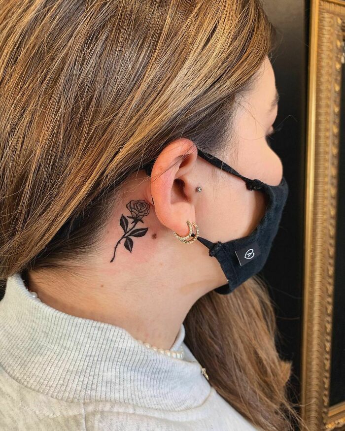 Woman with rose ear tattoo, wearing a mask, showcasing unique ear tattoo idea.