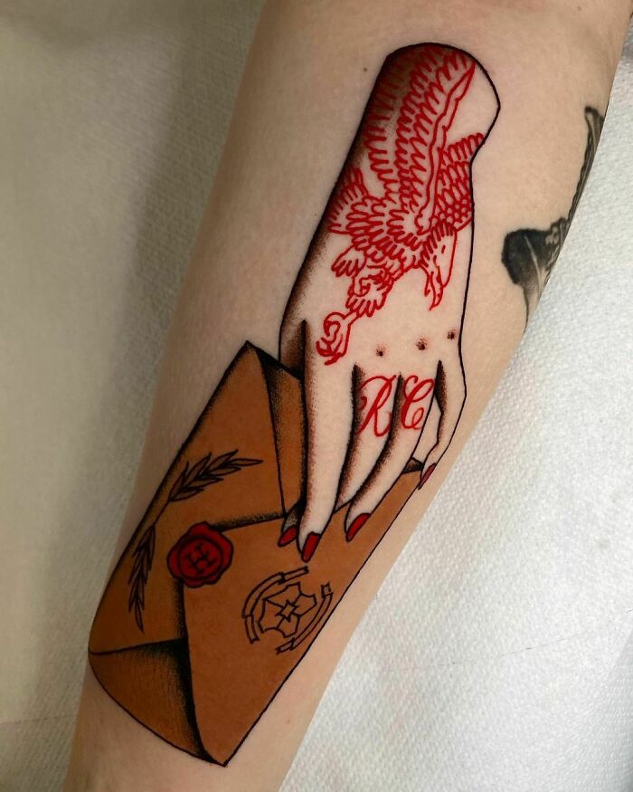 Tattoo of a hand with red eagle and initials "RC" holding a brown envelope, inspired by the Wizarding World.