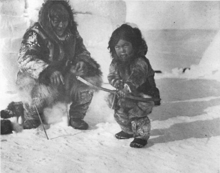 Hombre inuk enseñando a un niño a disparar. Alrededor de 1920
