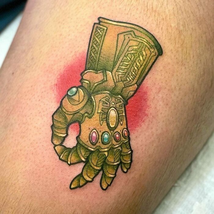 Marvel tattoos featuring an intricately designed Infinity Gauntlet with vibrant colors on skin.