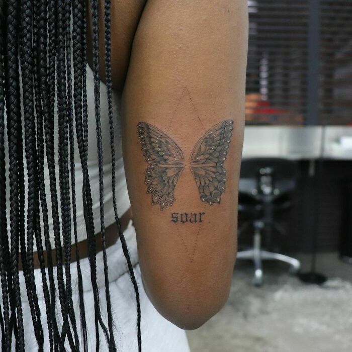 Butterfly word tattoo with "soar" on an arm, symbolizing freedom and inspiration.