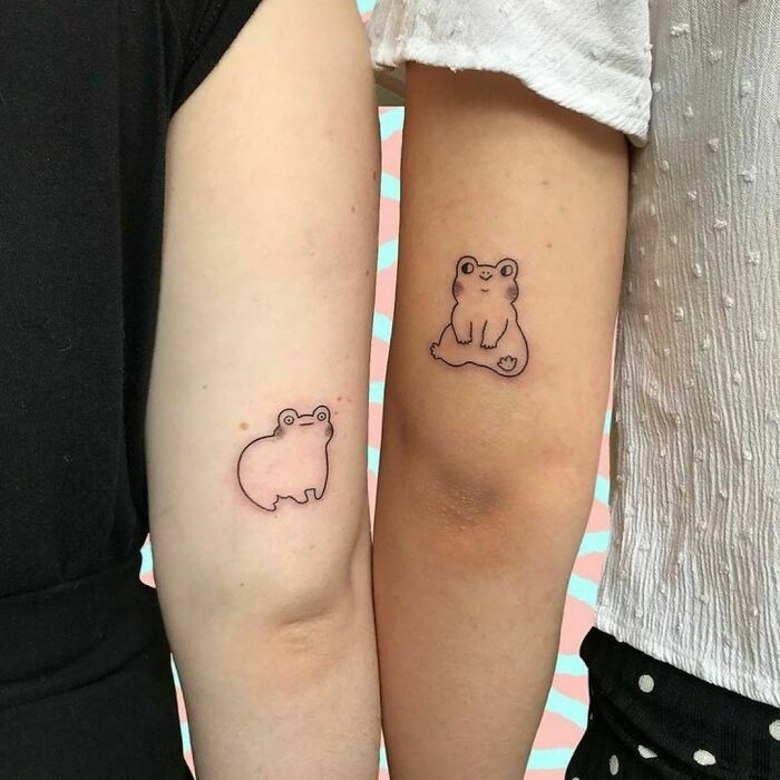 Two arms with minimalist frog tattoos symbolizing friendship.