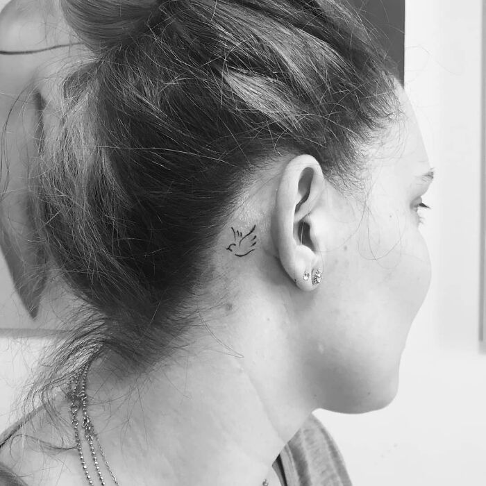 Woman with a small bird ear tattoo, showcasing subtle tattoo design behind the ear.