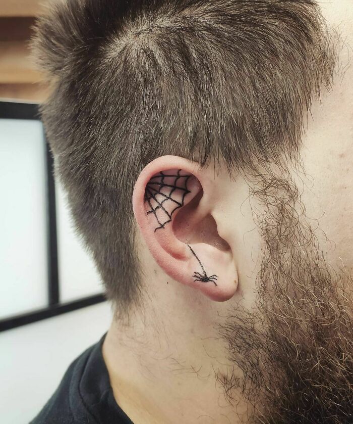 Ear tattoo featuring a delicate spider web design, elegantly situated on the upper ear.