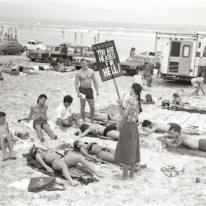 People laying in the beach and a woman with a sign standing near them 