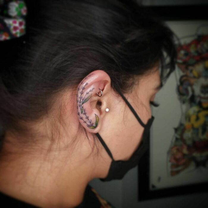 Intricate ear tattoo with floral design on woman's ear, featuring delicate leaves and flowers.