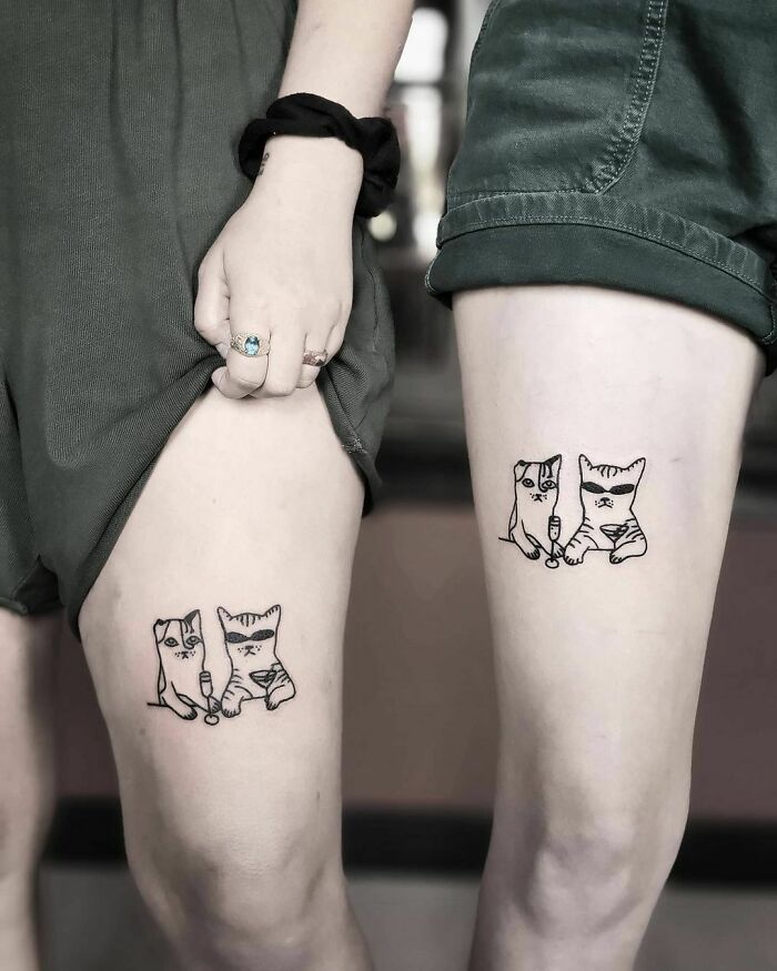 Two legs with best friend tattoos featuring two cartoon-style cats holding syringes, symbolizing friendship.