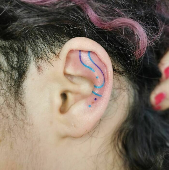 Colorful blue ear tattoo with abstract lines and dots behind the ear.