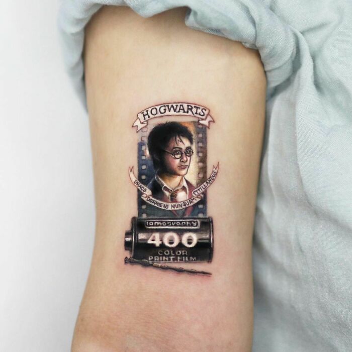 Harry Potter tattoo featuring film strip and Hogwarts banner on arm.