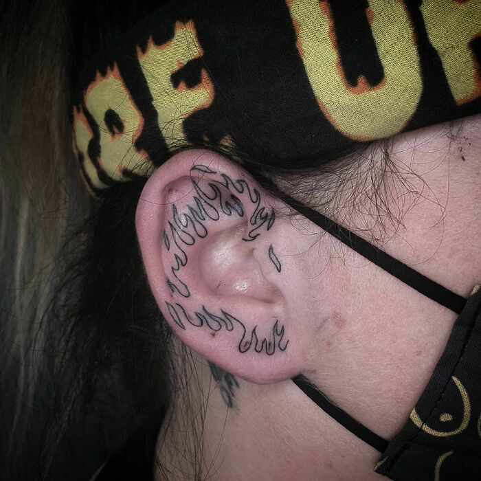 Black flame design ear tattoo on a person's ear, showcasing creative tattoo art style.