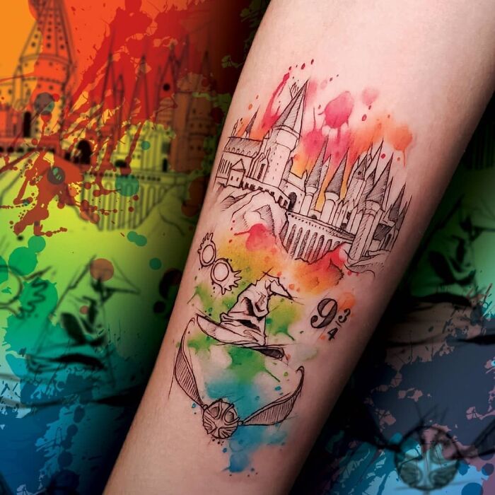 Colorful Harry Potter tattoo featuring Hogwarts, Sorting Hat, and Golden Snitch on an arm with abstract watercolor background.