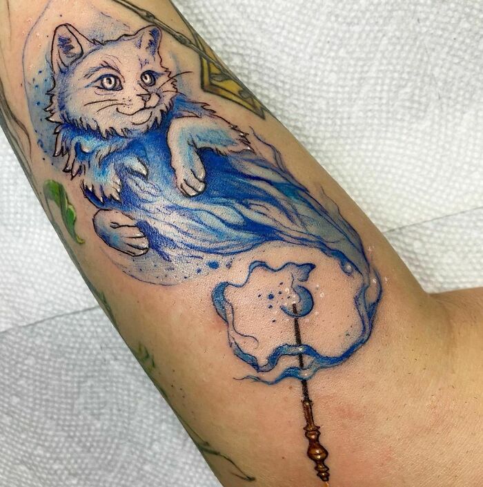 Harry Potter tattoo of a blue cat Patronus with a wand on an arm.