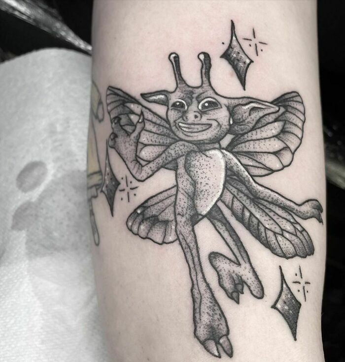 Harry Potter tattoo of whimsical creature with wings on the forearm, surrounded by sparkles.