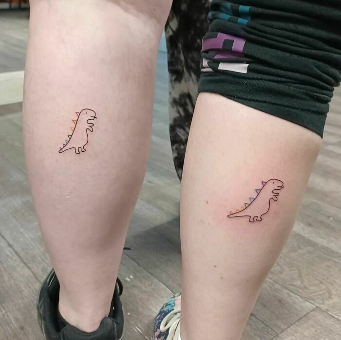 Matching dinosaur tattoos on two calves, symbolizing best friend friendship with minimalist design.
